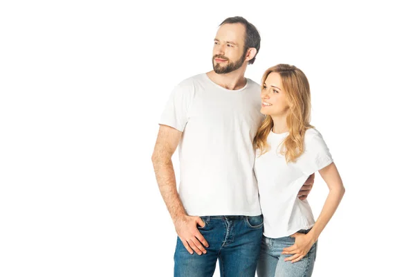 Alegre pareja adulta en camisetas blancas abrazando y mirando hacia otro lado aislado en blanco - foto de stock