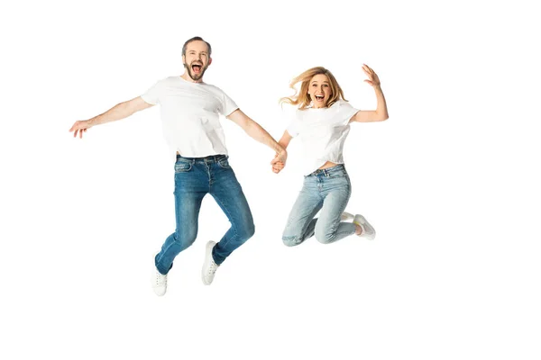 Happy adult couple in white t-shirts holding hands while jumping isolated on white — Stock Photo