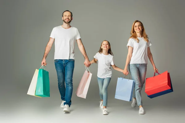Alegre familia caminando con coloridas bolsas de compras y tomados de la mano sobre fondo gris - foto de stock