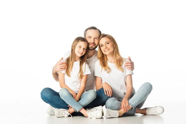 Felice famiglia seduta sul pavimento con le gambe incrociate e abbracciando isolato su bianco — Foto stock