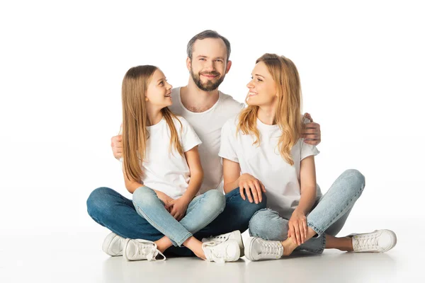 Happy family sitting on floor with crossed legs and embracing isolated on white — Stock Photo