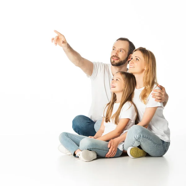 Familia feliz sentado en el suelo con las piernas cruzadas, mientras que el hombre apuntando aislado en blanco - foto de stock