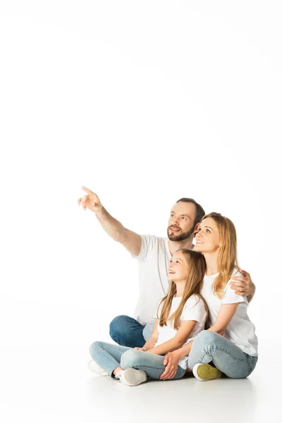 Happy family sitting on floor with crossed legs while man pointing away isolated on white — Stock Photo