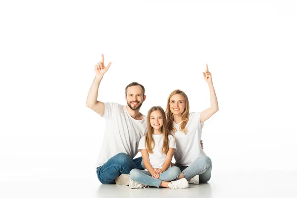Happy family sitting on floor with crossed legs and pointing up isolated on white — Stock Photo
