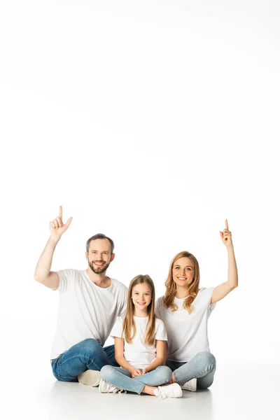 Família feliz sentado no chão com pernas cruzadas e apontando para cima isolado no branco — Fotografia de Stock