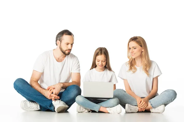 Parents sitting on floor near happy daughter with laptop isolated on white — Stock Photo