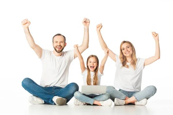 Excited parents sitting on floor near happy daughter with laptop isolated on white — Stock Photo