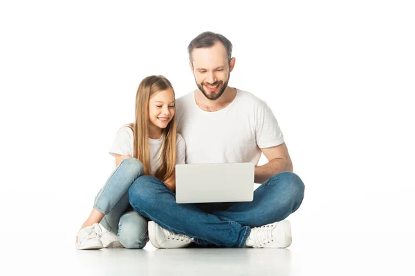 Усміхнений батько і дочка сидять на підлозі з ноутбуком ізольовані на білому — стокове фото