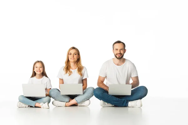 Fröhliche Familie sitzt auf dem Boden mit Laptops auf überkreuzten Beinen isoliert auf weiß — Stockfoto