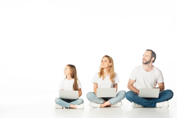 Família sentada no chão com laptops em pernas cruzadas e olhando para longe isolado no branco — Fotografia de Stock