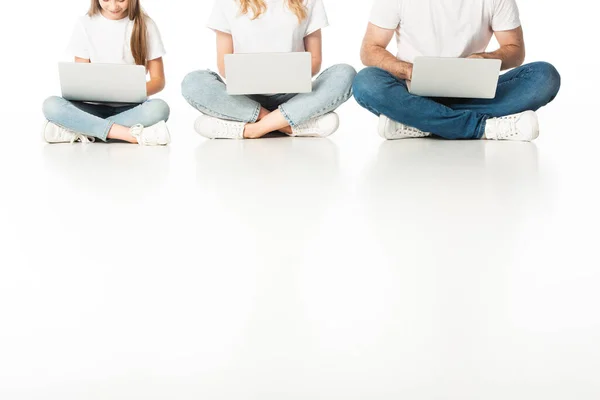 Vue recadrée de la famille assise sur le sol avec des ordinateurs portables sur les jambes croisées sur blanc — Photo de stock