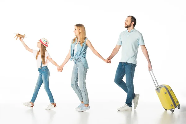 Familia feliz cogida de la mano mientras camina con bolsa de viaje aislada en blanco - foto de stock