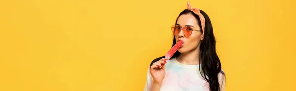 Stylish summer brunette girl eating ice cream isolated on yellow, panoramic shot — Stock Photo