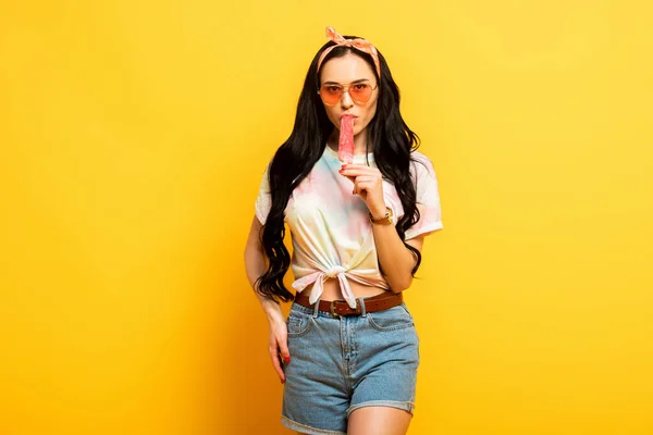 Chica morena verano elegante comiendo helado sobre fondo amarillo - foto de stock