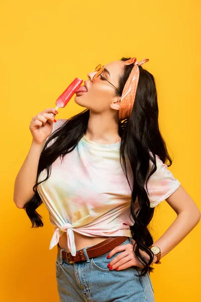 Stylish summer brunette girl licking ice cream on yellow background — Stock Photo