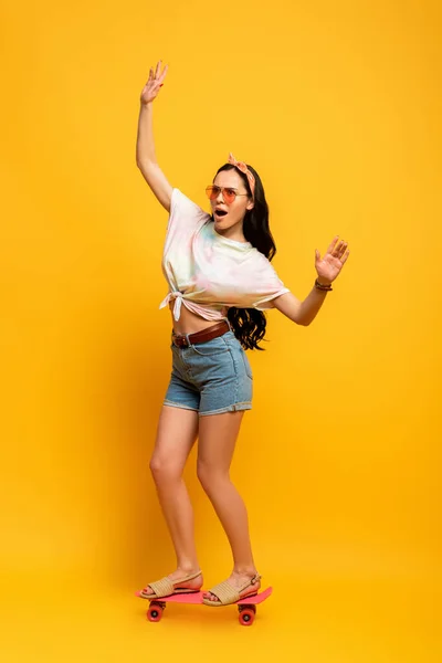 Schockiert stilvolle Sommer Brünette Mädchen Reiten rosa Penny Board auf gelbem Hintergrund — Stockfoto