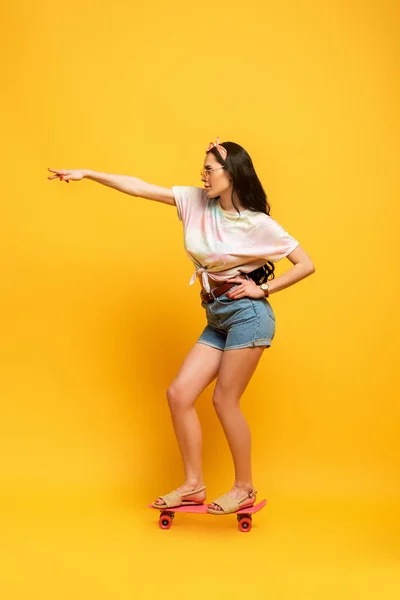 Élégant été brunette fille posant sur penny rose planche sur fond jaune — Photo de stock