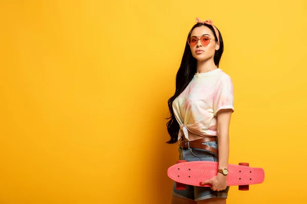 Stylish summer brunette girl with pink penny board on yellow background — Stock Photo