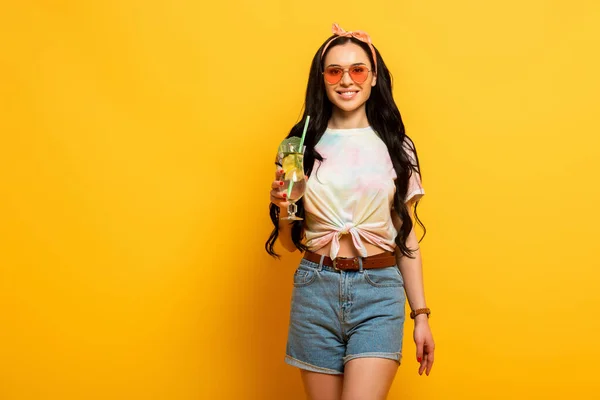 Усміхнена стильна літня брюнетка дівчина з освіжаючим коктейлем на жовтому фоні — стокове фото