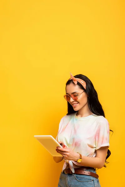 Smiling stylish summer brunette girl using digital tablet on yellow background — Stock Photo