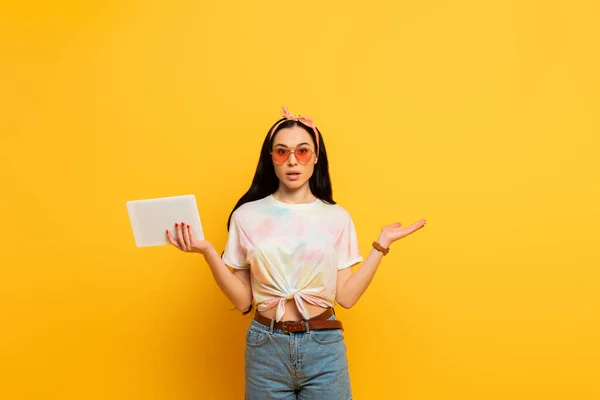 Verwirrt stilvolle Sommer Brünette Mädchen hält digitale Tablette auf gelbem Hintergrund — Stockfoto