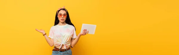 Смущен стильный летом брюнетка девушка держит цифровой планшет на желтом фоне, панорамный снимок — стоковое фото