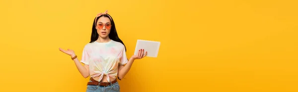 Confuso elegante verão morena menina segurando tablet digital no fundo amarelo, tiro panorâmico — Fotografia de Stock