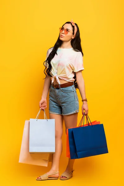Dreamy stylish summer brunette girl with shopping bags on yellow background — Stock Photo