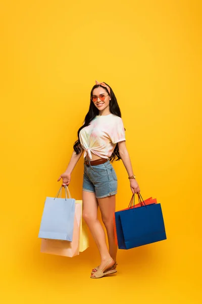 Lächelnd stilvolle Sommer Brünette Mädchen mit Einkaufstaschen auf gelbem Hintergrund — Stockfoto