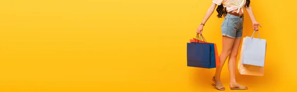 Cropped view of stylish summer girl with shopping bags on yellow background, panoramic shot — Stock Photo