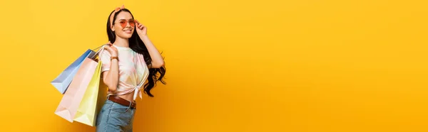 Sorridente ragazza bruna estate elegante con borse della spesa su sfondo giallo, colpo panoramico — Foto stock