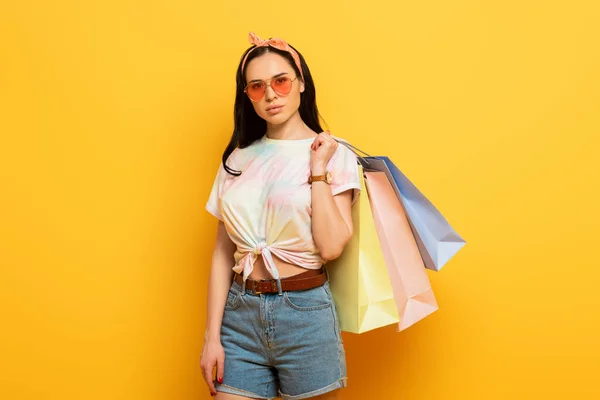 Ernste stilvolle Sommer Brünette Mädchen mit Einkaufstaschen auf gelbem Hintergrund — Stockfoto