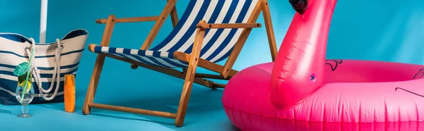 Close up view of striped deck chair near inflatable flamingo, sunscreen, beach bag and cocktail on blue background, panoramic shot — Stock Photo
