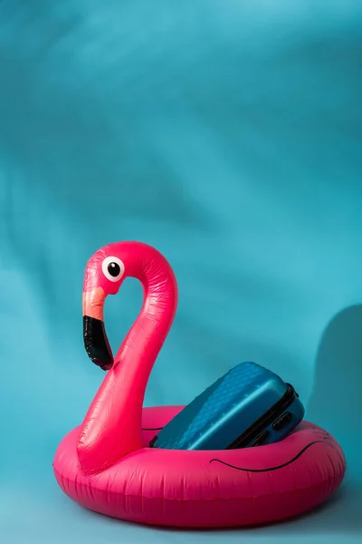 Pink inflatable flamingo and suitcase on blue background — Stock Photo