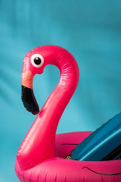 Rosa aufblasbarer Flamingo und Koffer auf blauem Hintergrund — Stockfoto