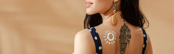 Vista cortada de mulher com sol desenhado feito de protetor solar e tatuagem nas costas no fundo bege, tiro panorâmico — Fotografia de Stock