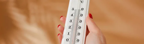 Vue recadrée d'une femme tenant un thermomètre sur fond beige, panoramique — Photo de stock
