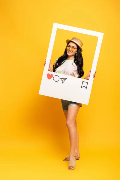 Усміхнена брюнетка дівчина в літньому вбранні позує в соціальній мережі на жовтому фоні — стокове фото