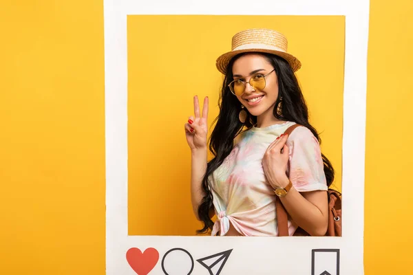 Happy brunette girl in summer outfit showing peace sign in social network frame on yellow background — Stock Photo