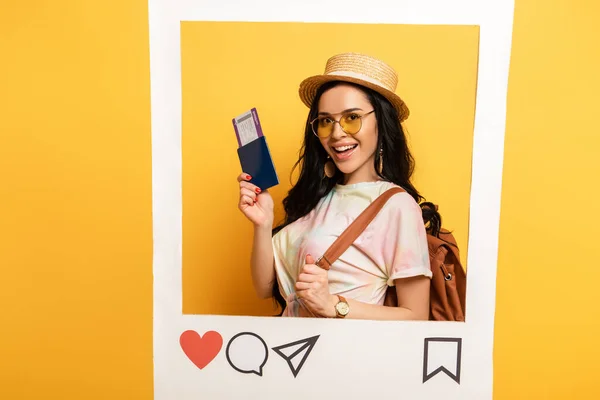 Glückliches brünettes Mädchen im Sommer-Outfit mit Flugticket im sozialen Netzwerk-Rahmen auf gelbem Hintergrund — Stockfoto