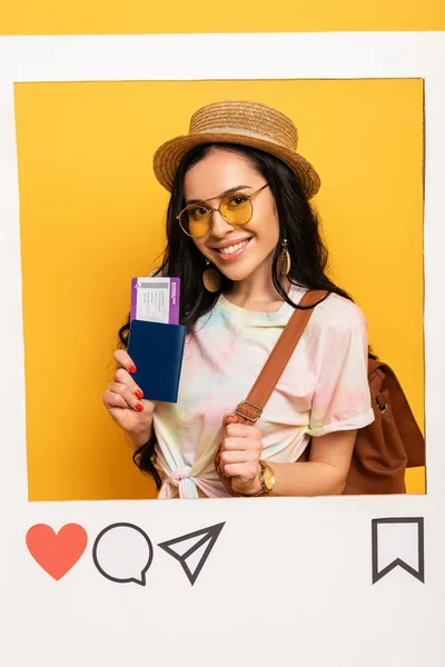 Happy brunette girl in summer outfit holding air ticket in social network frame on yellow background — Stock Photo
