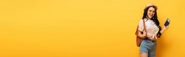 Glückliches brünettes Mädchen im Sommer-Outfit mit Flugticket auf gelbem Hintergrund, Panoramaaufnahme — Stockfoto