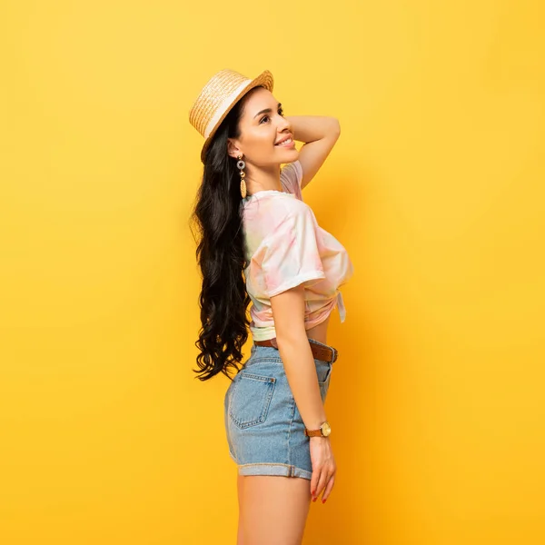 Side view of smiling brunette girl in straw hat on yellow background — Stock Photo