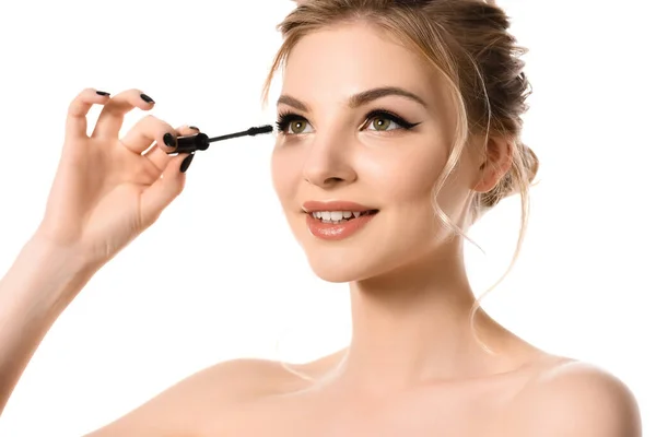 Sonriente mujer rubia hermosa desnuda con maquillaje y uñas negras aplicando rímel aislado en blanco - foto de stock