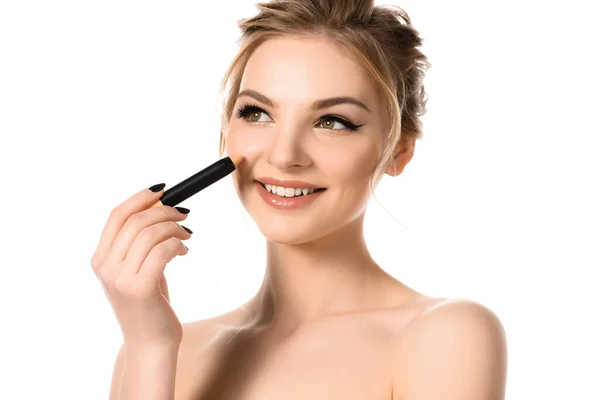 Sorridente bella donna bionda nuda con trucco e unghie nere applicando bastone correttore isolato su bianco — Foto stock