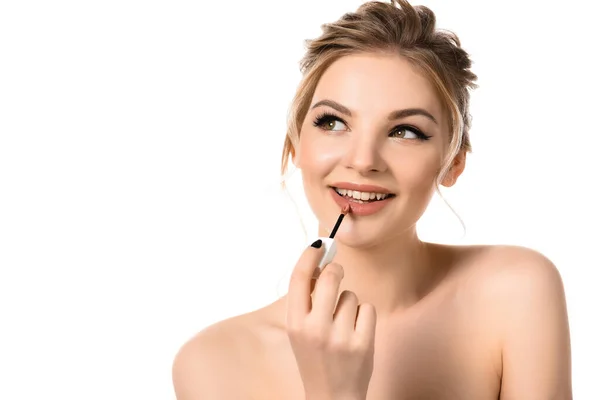 Sonriente mujer rubia hermosa desnuda con maquillaje y uñas negras aplicando brillo de labios beige aislado en blanco - foto de stock