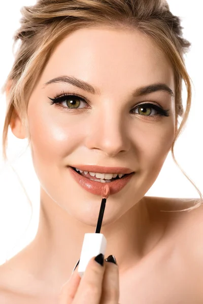 Sonriente mujer rubia hermosa desnuda con maquillaje y uñas negras aplicando brillo de labios beige aislado en blanco - foto de stock