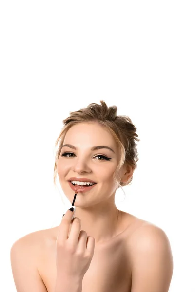 Sonriente mujer rubia hermosa desnuda con maquillaje y uñas negras aplicando brillo de labios beige aislado en blanco - foto de stock