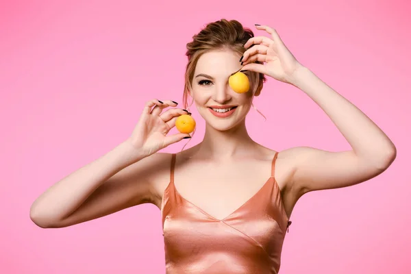 Smiling elegant beautiful blonde woman in silk dress holding apricots isolated on pink — Stock Photo
