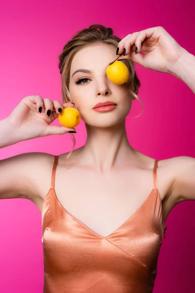 Elegante hermosa mujer rubia en vestido de seda sosteniendo albaricoques aislados en rosa - foto de stock